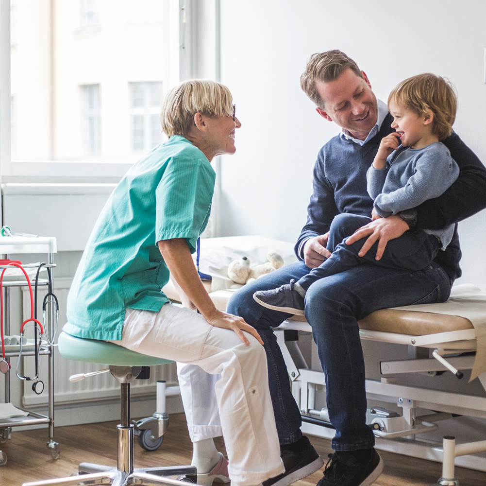 A smiling doctor in scrubs talks to a father and his son.